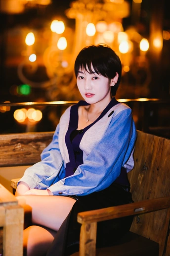 一个年轻女子坐在夜晚的 wooden bench 上 背景有灯光。