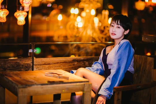 一个年轻女子坐在夜晚的餐厅或酒吧里的木凳上