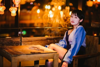一个年轻女子坐在夜晚的餐厅或酒吧里的木凳上