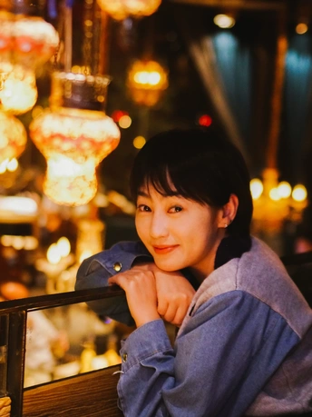 一个年轻女子坐在餐厅的桌子旁 背景有灯光。