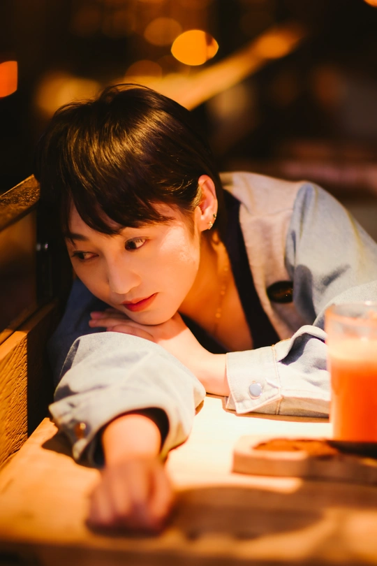 一个年轻女孩坐在餐厅的桌子旁 手里拿着一杯饮料 一个小男孩正看着她。