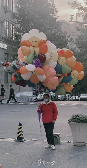 一个人戴着面具走过街头卖气球的商贩。