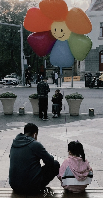 一个男子和一名女子坐在长凳上 长凳上有一个小女孩和一只形状像花的气球。