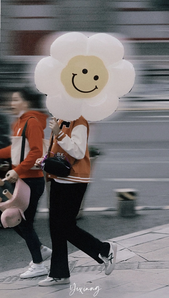 一个背着书包 头上戴着一只带着笑脸的泰迪熊的女孩走在街上。