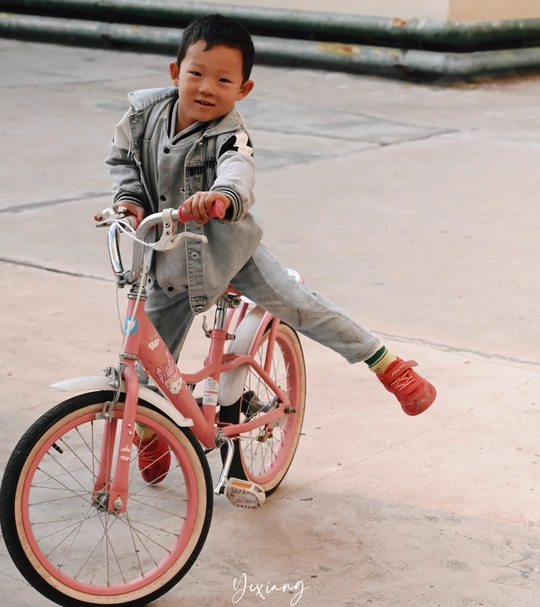 一个小男孩骑着一辆红色的自行车 旁边有一个小孩子。