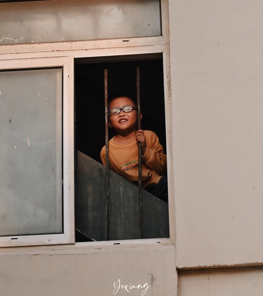 戴眼镜的女孩正在一栋建筑物的开窗处向外看