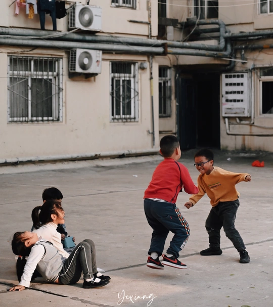 年轻人正在破旧的建筑物前街上踢足球或打棒球。