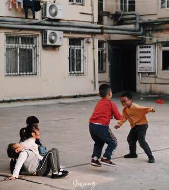 年轻人正在破旧的建筑物前街上踢足球或打棒球。