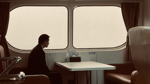 一个坐在火车座位上的男人正在看着窗外的一个女人坐在桌子旁