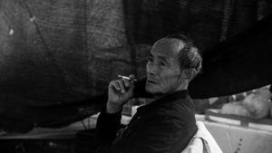 一张黑白照片 一位老人站在伞下抽烟。