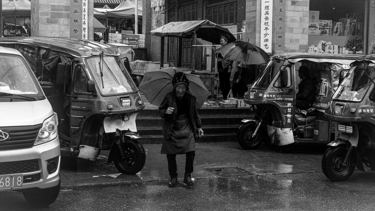 一张黑白照片 街道上停着车 人们在雨中行走