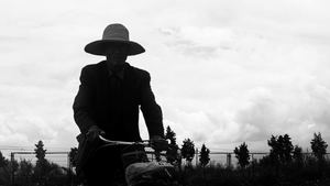 一张黑白照片 一个戴帽子的人在田地里骑自行车。