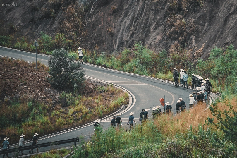 一些人正沿着一座山附近的路边走