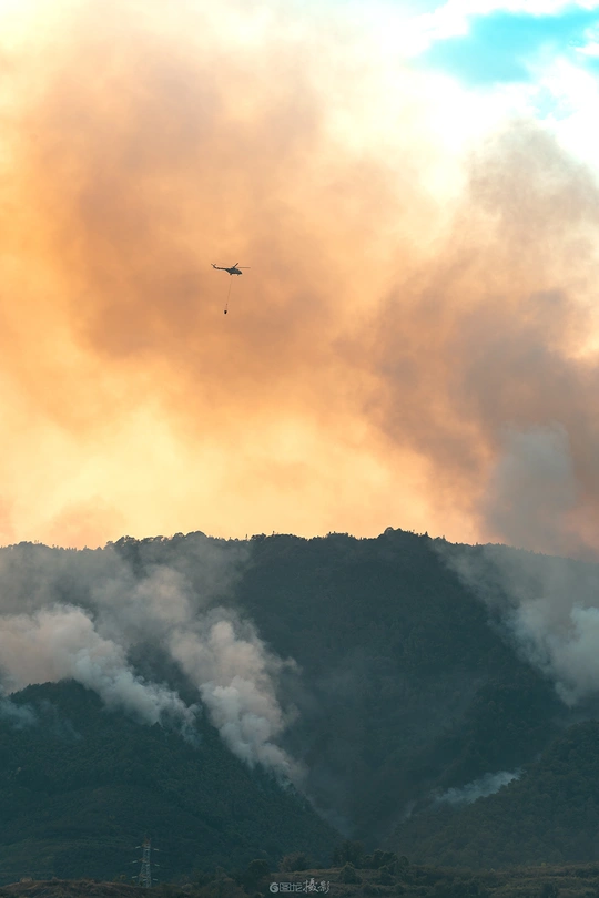 一架飞机在山丘上方的天空中飞行 身后有一大片烟雾