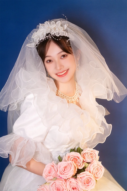 一位年轻女子穿着白色连衣裙和头纱 手拿粉色玫瑰花束的肖像。