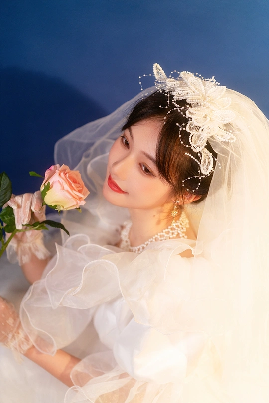 一位年轻女子穿着白色连衣裙和头纱 手拿玫瑰的肖像。