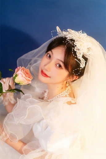 一位穿着白色连衣裙和面纱的年轻女子 手持玫瑰 在蓝色背景前摆姿势照相。