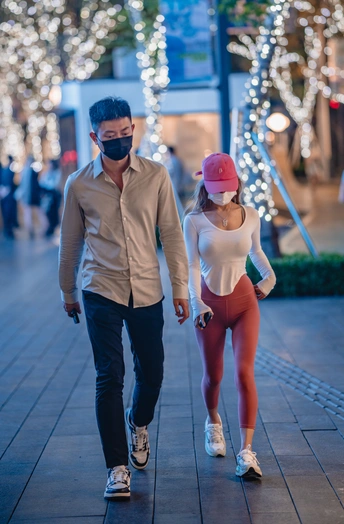 一对戴着口罩的年轻男女晚上手牵着手走在人行道上