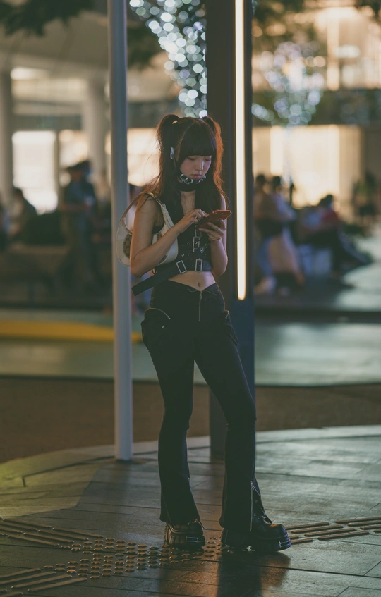 一名年轻女子靠在电线杆上 给另一个人看手机拍照