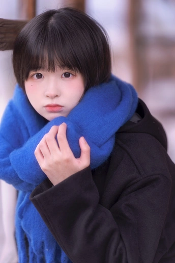 一位穿着蓝色围巾和外套的年轻女子站在雪中