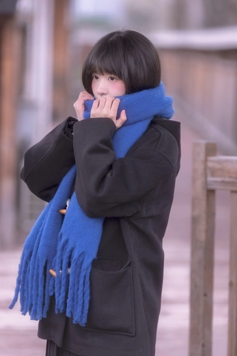 一个戴黑色外套和蓝色围巾的年轻女子在打电话时遮住了脸。