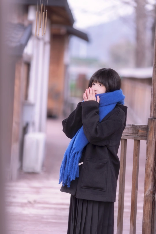 一个年轻女子站在门廊上用围巾遮住脸