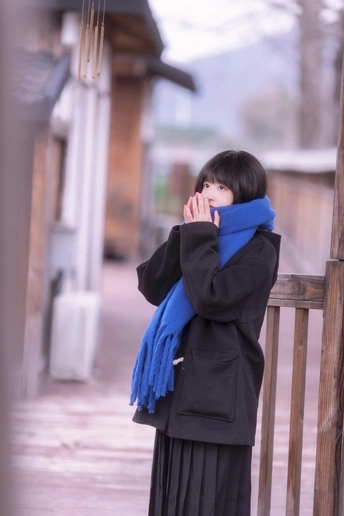 一个年轻女子站在门廊上用围巾遮住脸