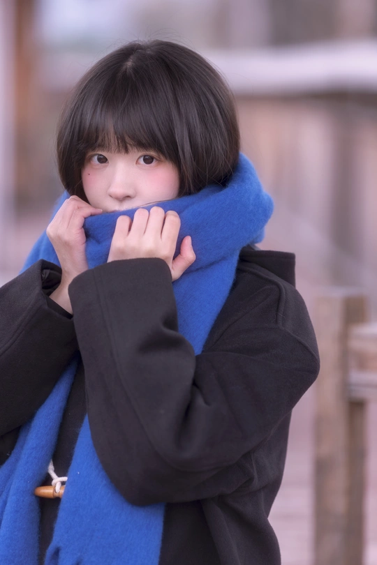 一位年轻女子穿着一件蓝色外套和围巾 用双手遮住脸。