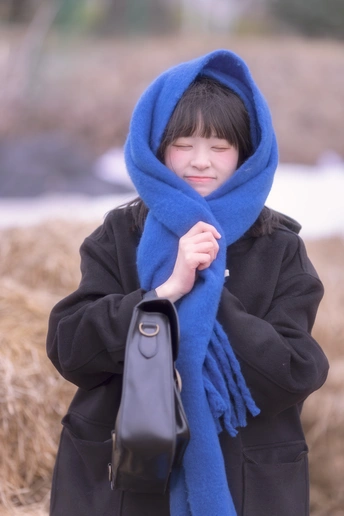一个穿着黑色外套和蓝色围巾的年轻女孩 holding a black bag