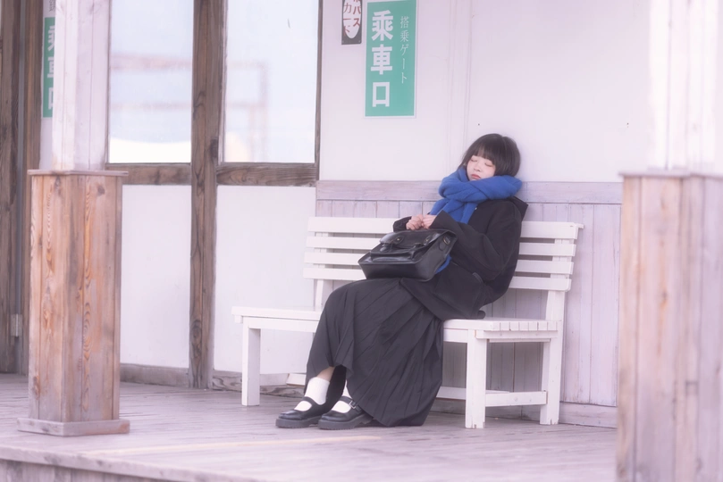 一个年轻的男孩坐在建筑物外的白色长凳上 而一个女人正在小憩。