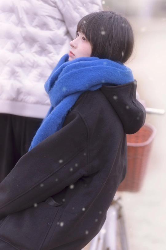 一位穿着蓝色外套和围巾的年轻女子站在雪中 手里拿着一把雨伞。