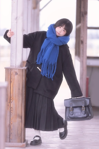 一位穿着黑色外套和蓝色围巾的女士拿着一个包