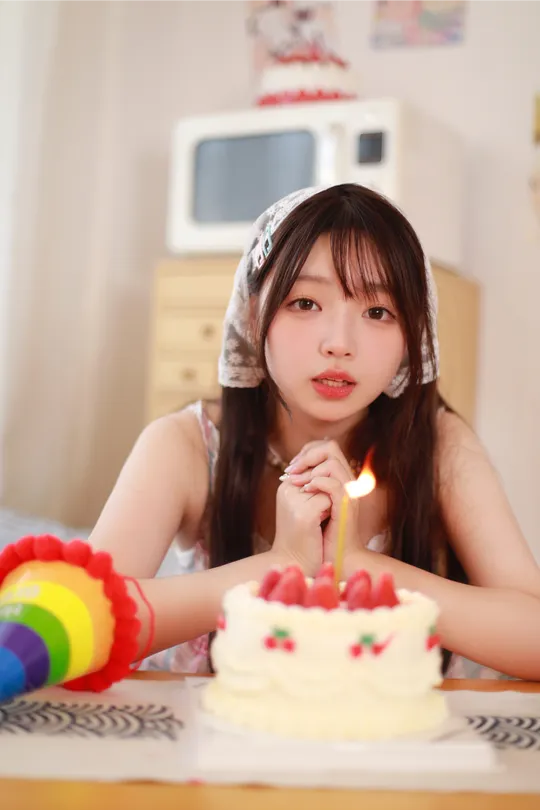 一个年轻女子坐在生日蛋糕前 蛋糕上的蜡烛都点着了。