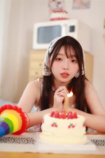 一个年轻女子坐在生日蛋糕前 蛋糕上的蜡烛都点着了。