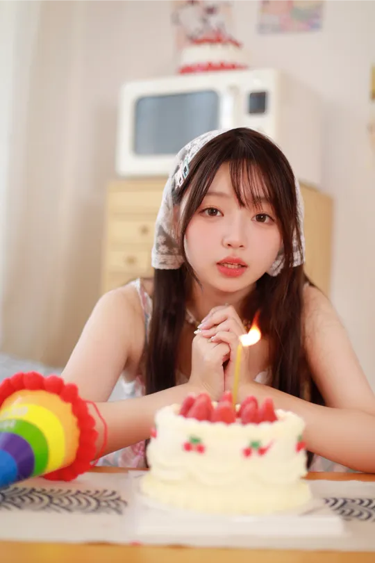 一个年轻女子坐在生日蛋糕前 蛋糕上的蜡烛都点着了。