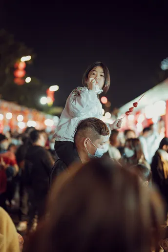 一个人戴着面具 在夜晚的节日人群中抱着一个小女孩。