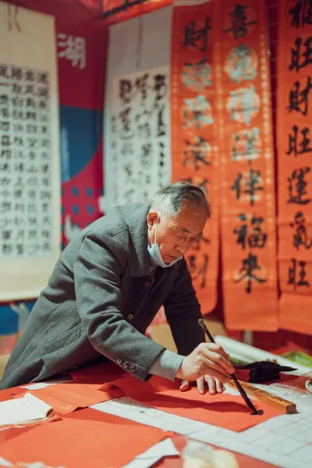 一个老人在一个带有书法的红色桌子旁工作