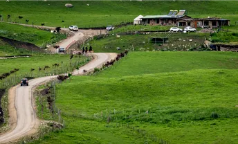 一辆驶过乡村小路的汽车 背景是绿山和房子。