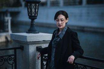 一位年轻女子穿着一件外套站在一座河上的桥上