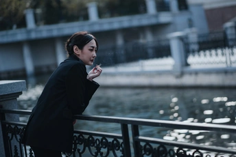 一个穿着外套的年轻女子站在桥上 抽着烟。