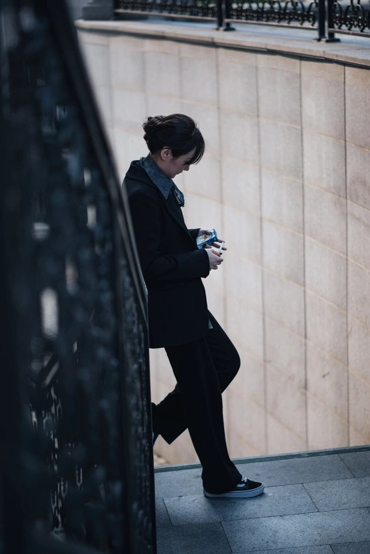 一位女士站在墙边 正看着她的手机 此时一名男子经过。
