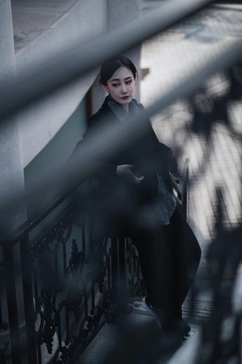 一位年轻女子穿着一件外套站在楼梯旁边的一道围墙旁边