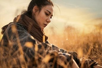 夕阳下坐在麦田中的青青草地上的年轻女子