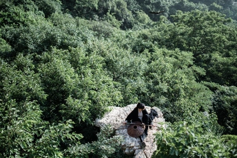 一个坐在森林中间一块岩石上的男人 背景中有树木和山脉。