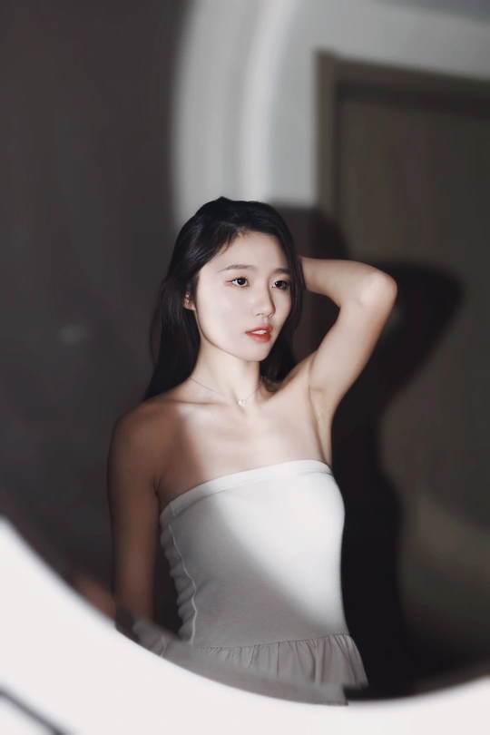 一位穿着白色连衣裙的年轻女子正在镜子前看自己的倒影