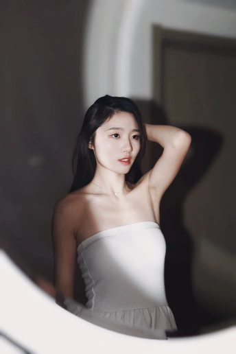 一位穿着白色连衣裙的年轻女子正在镜子前看自己的倒影