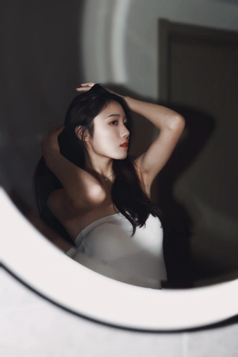 一位年轻女子站在一个圆形的镜子前 向外看窗。