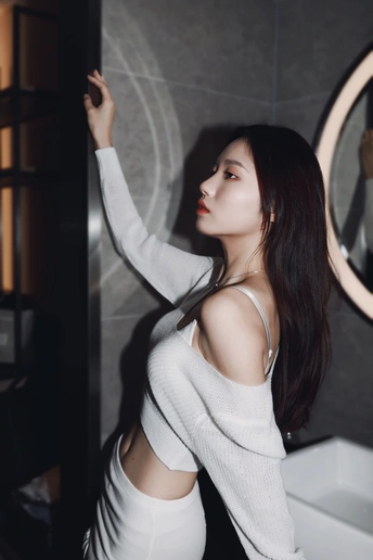 一位穿着白色衣服的年轻女子在浴室镜子前摆姿势