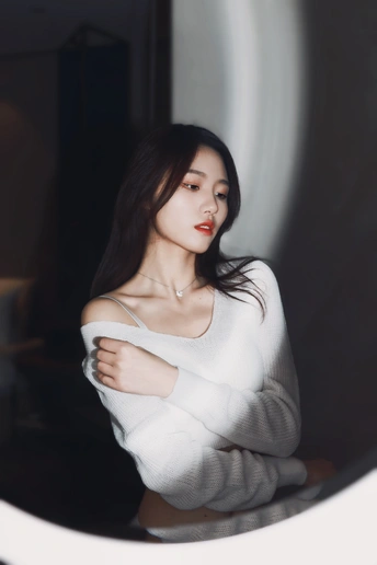 站在镜子前的穿着白色毛衣的年轻女子