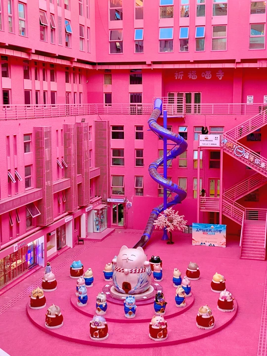 一座粉红色的建筑 有一个带纸杯蛋糕和蓝色雕塑的大庭院